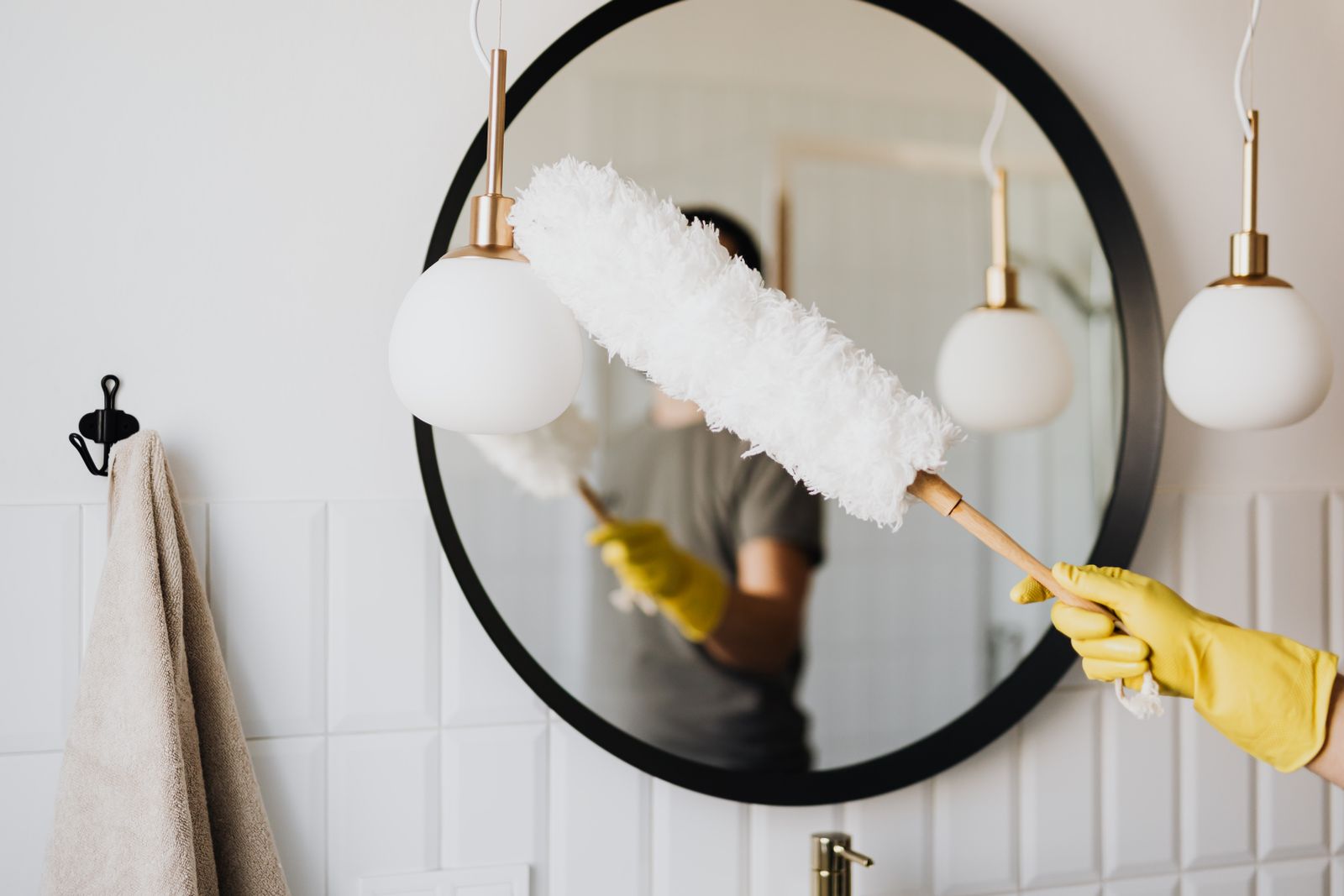 Cleaner wearing yellow gloves dusting bathroom fixtures